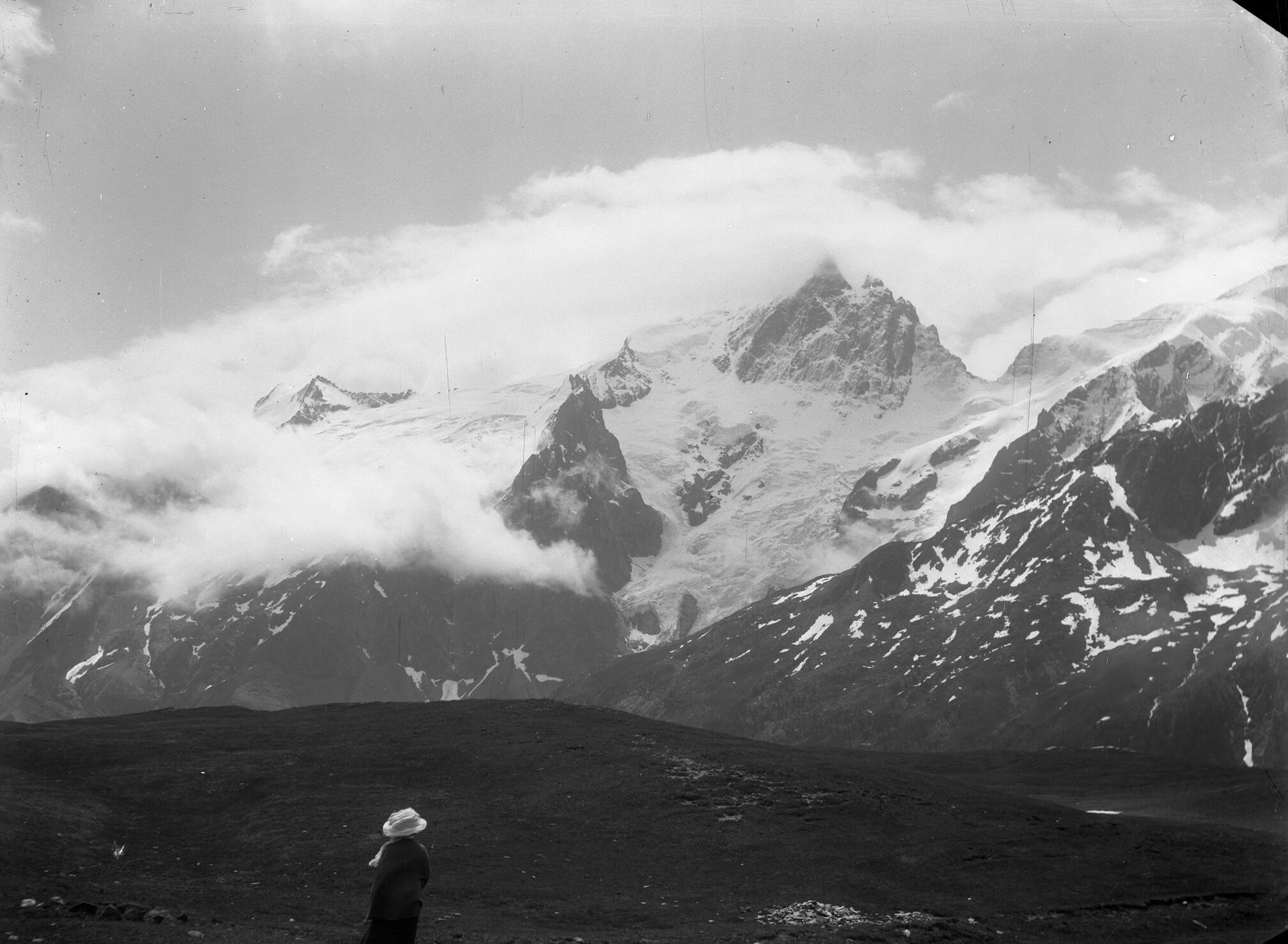 Une femme admire la Meije, enveloppée de nuages, depuis le plateau d'Emparis, côté La Grave.