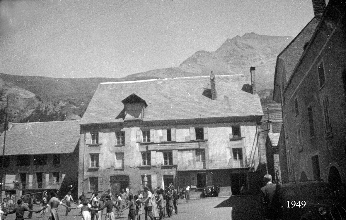 Vue place devant Bec de l'Homme. Un groupe de touristes fait une ronde tandis qu'une voiture est garée à l'ombre. Au fon