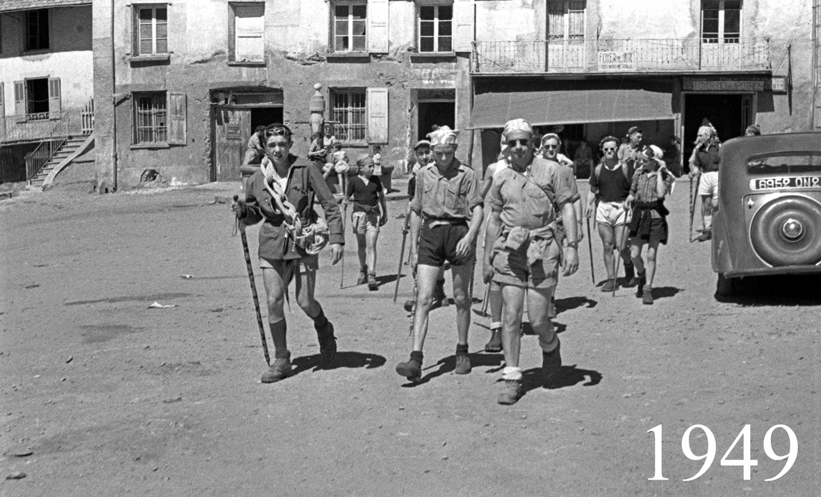 Prise pendant l'été 1949, ce cliché montre un groupe de randonneurs partant de la place du village, avec en fond le Bec 
