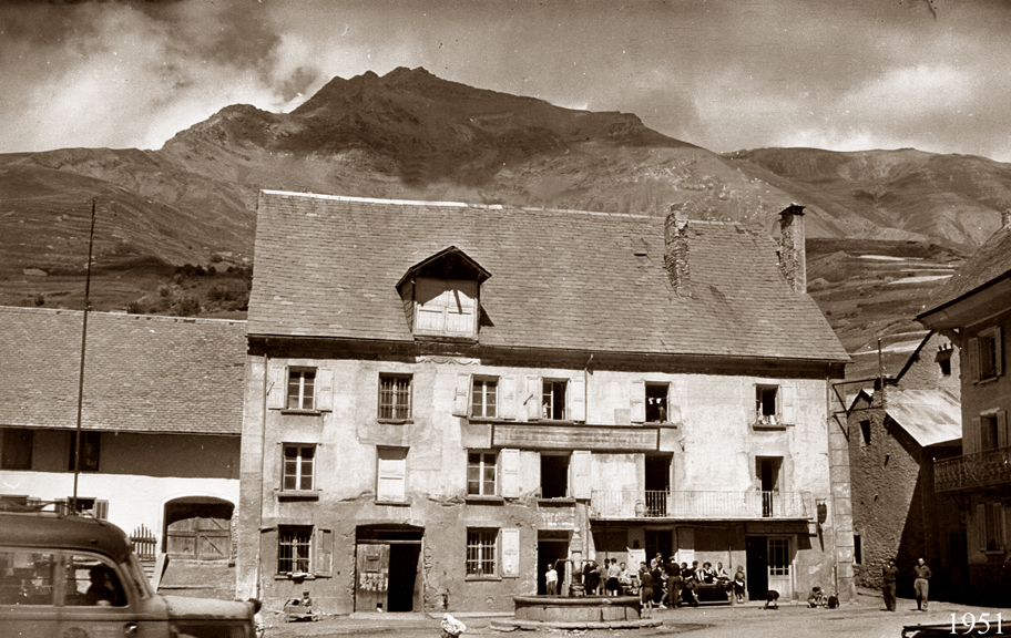 Scène de la vie d'autrefois avec un groupe de personnes assis à la terrasse du Bec de l'Homme en 1951 tandis qu'une voit