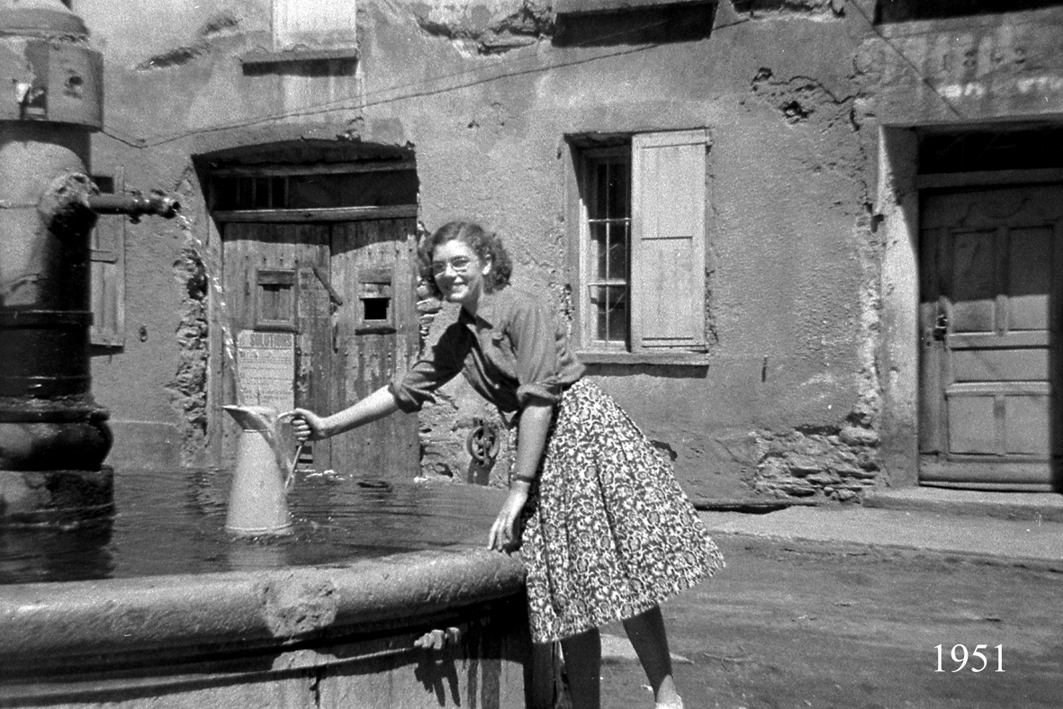 Jeune femme remplissant son pichet l'eau à la fontaine devant le Bec de l'Homme en 1951.
